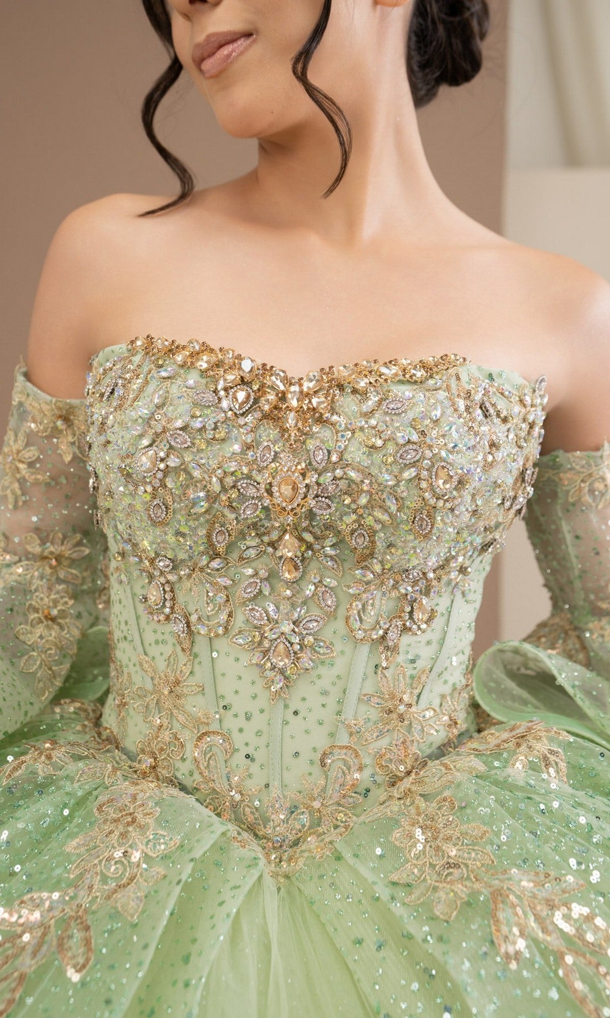 A woman wears the Quinceanera Dress 8575JQ by Cinderella Couture, a light green off-the-shoulder ball gown adorned with gold embroidery, beading, and sequins.
